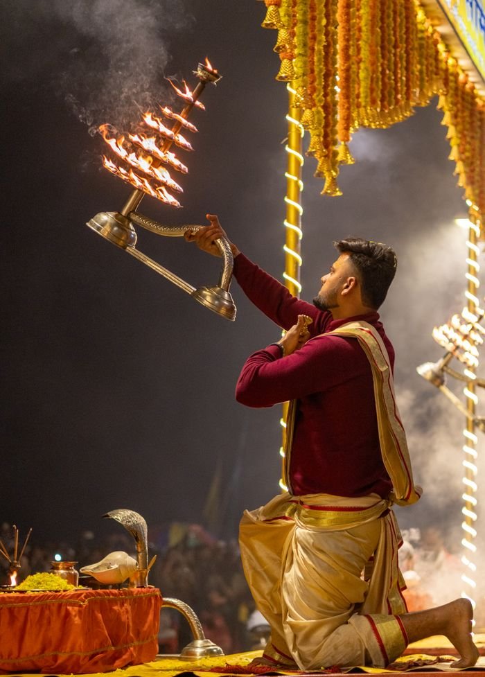 A priest performs Ganga Aarti at night in Varanasi, India, with traditional lamps.